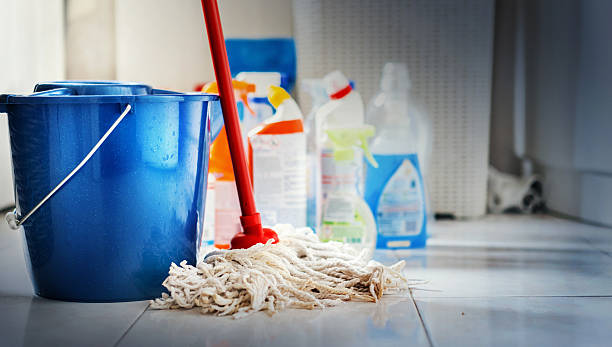 Cleaning products. Closeup of unrdcognizable home cleaning products with blue bucket and a mop in front in sharp focus. All products placed on white and poorly lit bathroom floor. mop photos stock pictures, royalty-free photos & images