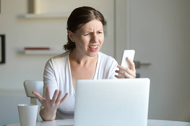 retrato de una mujer el portátil, mirando la pantalla del móvil - shock surprise people business fotografías e imágenes de stock