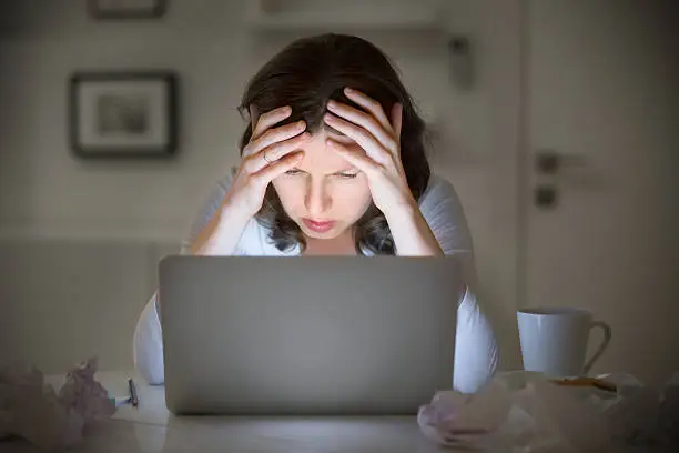 Portrait of a woman grabbing her head in despair at the desk near the laptop, late at night. Education, business concept photo. Lifestyle