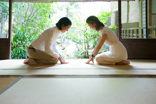 Two Japanese women bowing with respect in a traditional house.