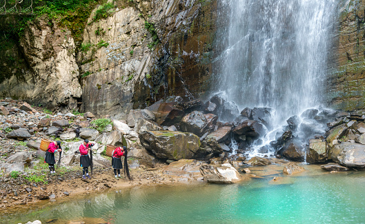 Group of three Yao tribe women in traditional clothes washing in their typical ritual their famous extreme long dark hair at a natural waterfall in the mountains close to Ping An and Longsheng, Guilin - Guangxi, China.