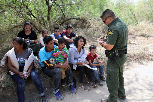 McAllen, Texas, USA - September 21, 2016: A Border Patrol agent takes a group of Central Americans into custody for illegally crossing the Rio Grande River into the U.S. in deep south Texas. There has been a flood of mothers with children and unaccompanied minors from Central America fleeing gang violence crossing illegally over the past several months.