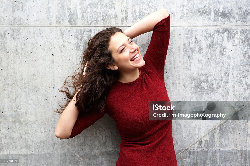 Séduisante jeune femme riant contre le mur gris - Photo de A la mode libre de droits