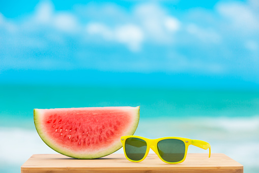 Slice of watermelon and pair of sunglasses on a sunny day at the beach.