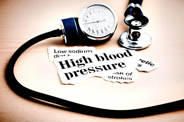 Headlines on high blood pressure and strokes on a wooden desk with part of  a blood-pressure gauge and a stethoscope.