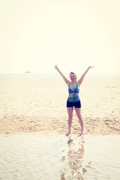 istock Woman stands on the sandy beach in a bathing suit 615821842