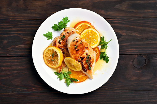 Grilled chicken breast with orange sauce on wooden background, top view