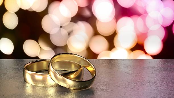 istock Two golden wedding rings on black table colored bokeh background 615824984