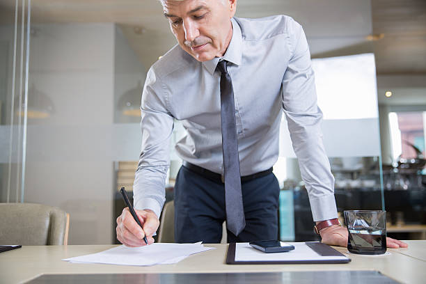 istock Senior Businessman Bending over Desk and Writing 615828610