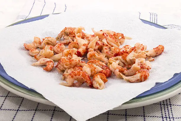 cleaned and cooked crayfish tails with white kitchen paper on a blue plate