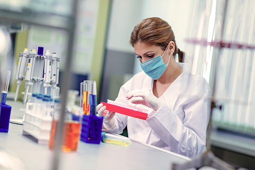 Woman in laboratory, examining new potions for the scientific research at university. Woman is wearing protective mask and protective gloves (Surgical gloves) while working with beakers, test tubes and other lab equipment. Series of images, taken with Nikon D800 and 50mm or 85 mm professional lens, developed from RAW. Focus on test tubes and hands, face out of focus