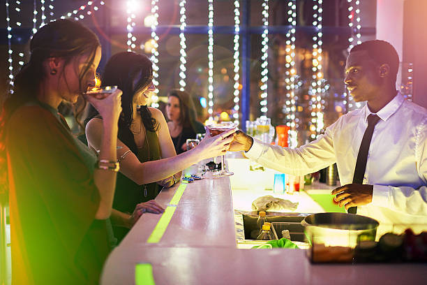 This one is on the house Shot of a barman handing a drink to a young woman over the bar counter cocktail bar busy stock pictures, royalty-free photos & images