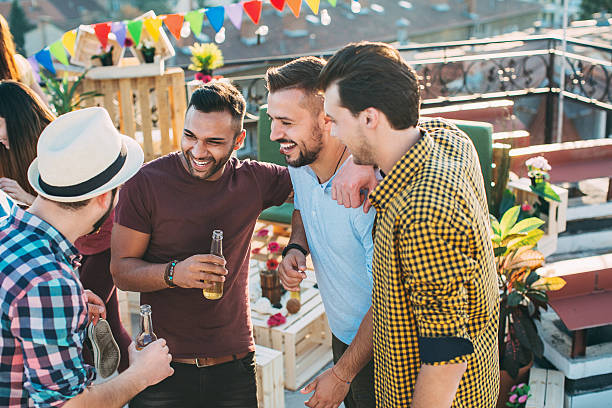 Group of male friends chatting and drinking Group of young men chatting and drinking beer on a rooftop party. stag night stock pictures, royalty-free photos & images