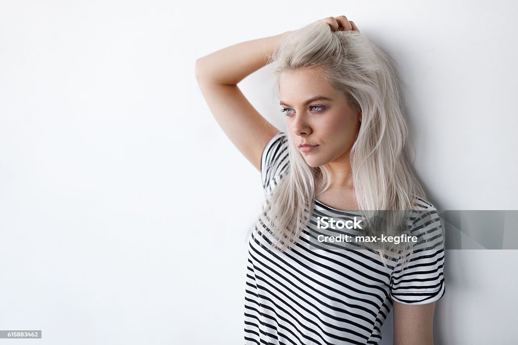 beautiful young blond woman posing while leaning on white wall beautiful young blond woman posing while leaning on white wall with copy space. Hipster girl with blue eyes and bleached silver hair Bleached Hair Stock Photo