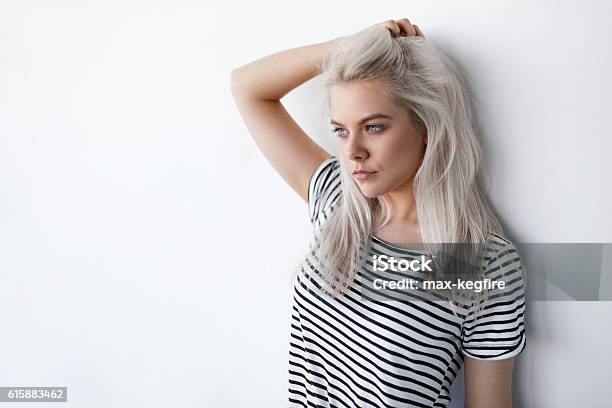 Beautiful Young Blond Woman Posing While Leaning On White Wall Stock Photo - Download Image Now