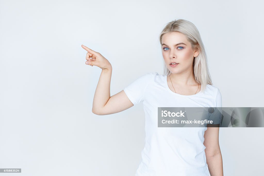 teenage girl in white t-shirt pointing finger away advertisement and people concept. young woman or teenage girl in white t-shirt pointing finger away to copy space isolated on grey background White People Stock Photo