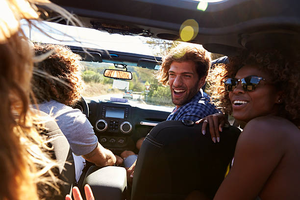 istock Four friends driving in an open top car, rear passenger 615885592
