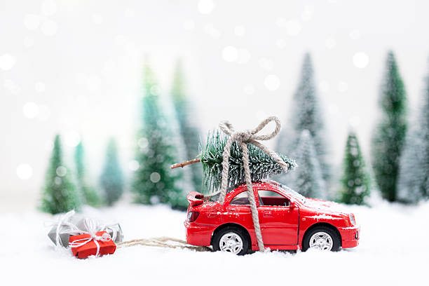 foresta invernale con auto rossa in miniatura che trasporta un albero di natale - schneelandschaft foto e immagini stock