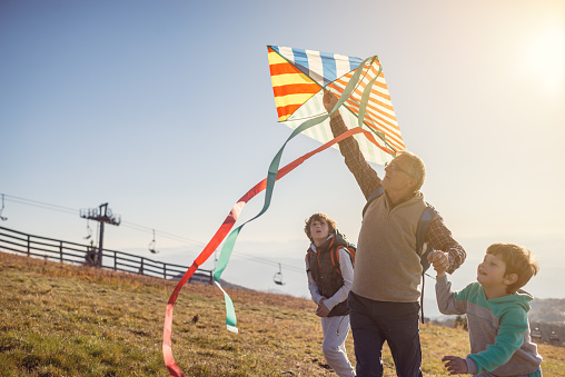 Grandfather flying a kite with his grandsons on mountain.They wear casual clothes and enjoy in great sunny day in nature.