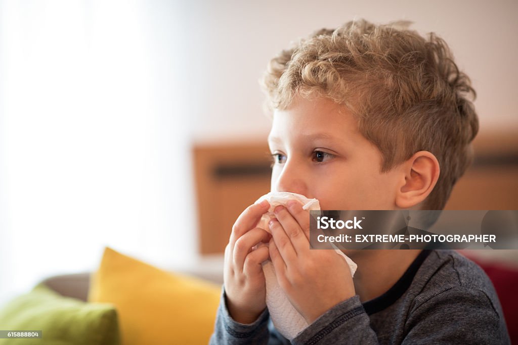 Little boy blowing nose Little boy with flu virus sitting on the sofa and wiping his nose with a napkin. Boys Stock Photo
