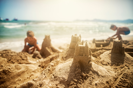 Two little brothers are building sandcastles. Sunny summer day.