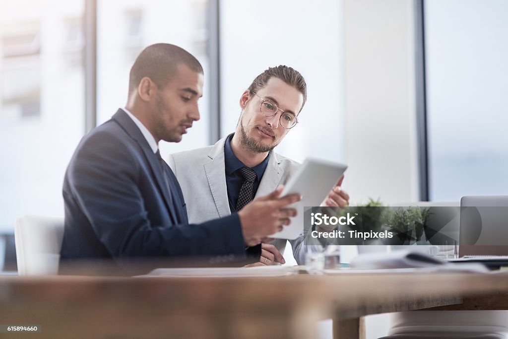 Meeting their business goals as a team Shot of two young businessmen using a digital tablet together at work Businessman Stock Photo