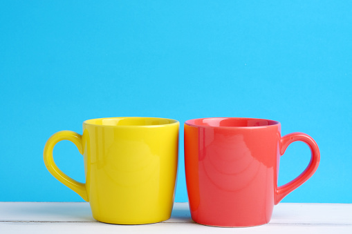 Close up of two cup yellow and red on white wood table and blue background concept, with blank space.