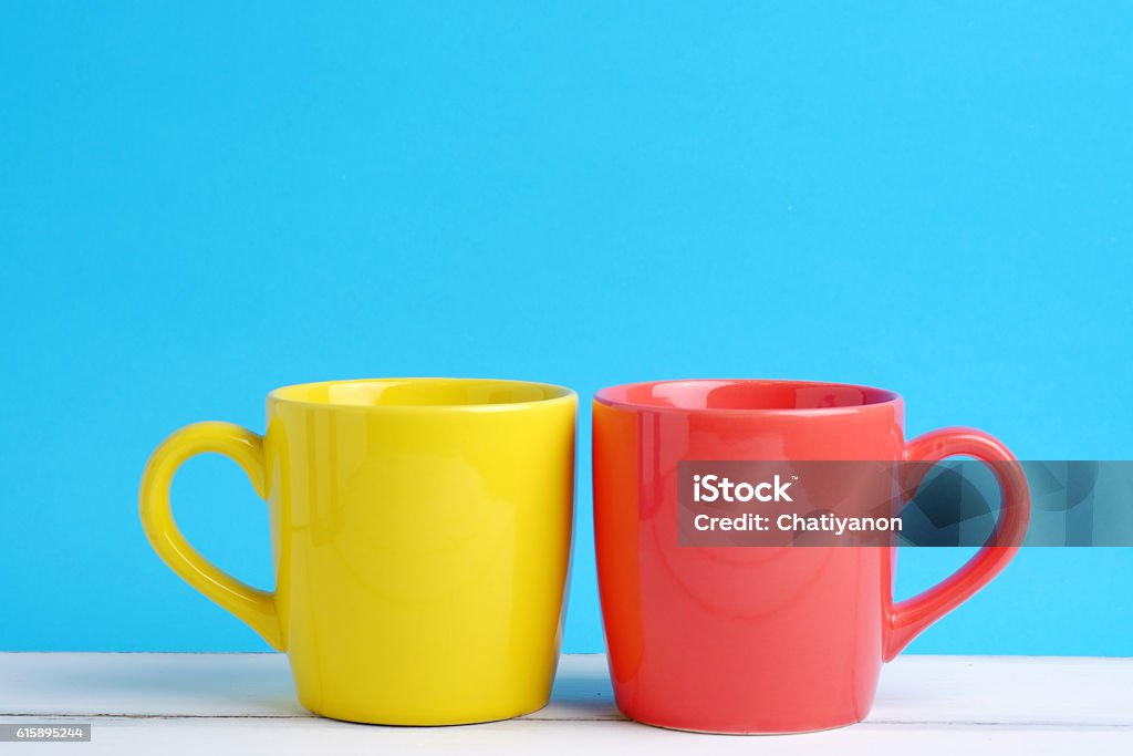 Yellow and red cup. Close up of two cup yellow and red on white wood table and blue background concept, with blank space. Two Objects Stock Photo