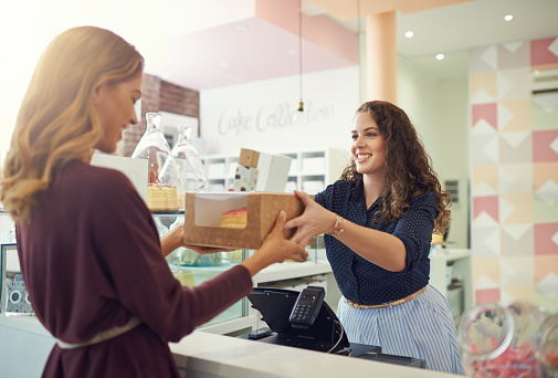 Shot of a young woman handing a box to a customer in her cake shop