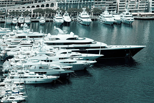 Monte Carlo, Monaco - July 30, 2015: A large luxury motor yacht in Monaco marina surrounded by smaller moored luxury yachts. In the background are other luxury vessels with apartments and hotels on the hillside.