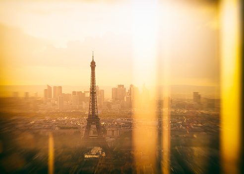 Sunset cityscape of Paris with the Eiffel Tower, Champs de Mars and business district La Defense at sunset, from elevated position with window reflections. Warm toned image with great copy space.