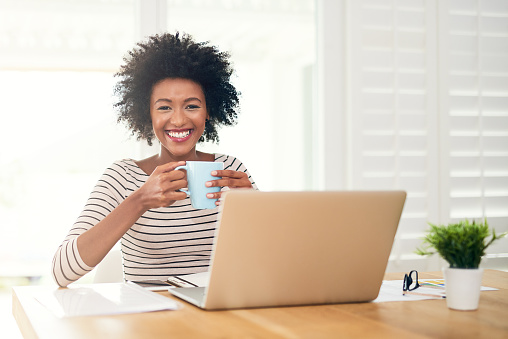 Portrait of a young woman drinking coffee while working on her laptop at home