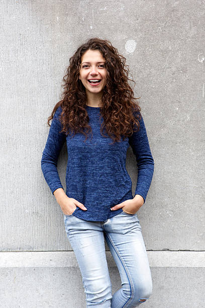istock Stylish young female model leaning to gray wall and smiling 615909436