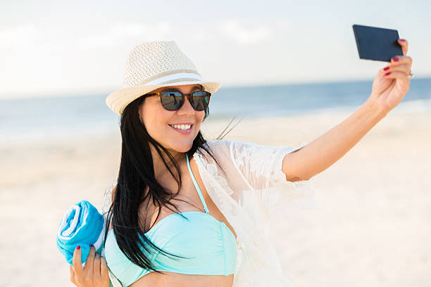 красивая женщина в солнцезащитных очках делает селфи на пляже - vacations photographing brown hair 30s стоковые фото и изображения