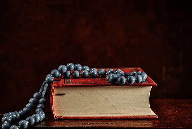 Rosary beads and red Holy Bible on table