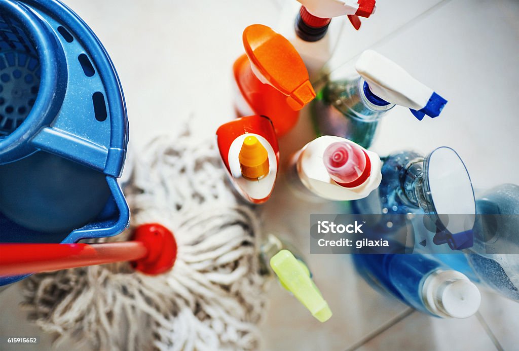 Cleaning products. Closeup top view of unrecognizable home cleaning products with blue bucket and a mop on the side. All products placed on white tiled bathroom floor. Cleaning Stock Photo