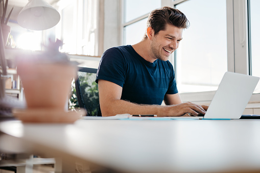 Happy young businessman using laptop at his office desk. Young male executive working on laptop at his desk.