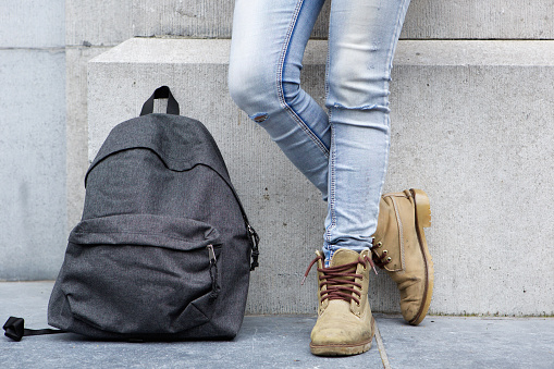 Low section portrait of backpack on sidewalk with female standing by