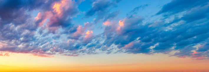 Panoramic photo of Cumulus Humilis, Stratocumulus clouds with warm highlights and blue sky at sunset.