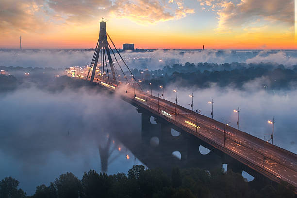 An ethereal scene unfolds on a misty morning in Istanbul as the first light of dawn breaks through the fog. The iconic Yavuz Sultan Selim Bridge emerges from the hazy atmosphere, its towering pillars shrouded in mystery. A cargo ship gracefully glides beneath the bridge, leaving a gentle wake in the calm waters of the Bosphorus. This captivating photograph captures the serenity and mystique of Istanbul's maritime landscape, where ancient and modern elements converge in perfect harmony. The soft, diffused light adds an enchanting touch to the scene, evoking a sense of tranquility and wonder in the viewer's heart