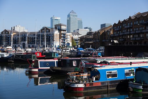 London, England - April 23, 2015:  Canary Wharf Viewed from Limehouse Basin, canal boats and barges are reflected in the water. Buildings and yachts can be seen. 