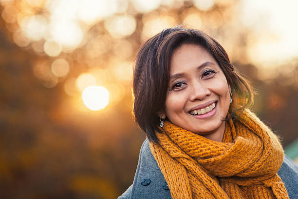 Autumn portrait of a woman A smiling woman in her 40s outdoors in autumn, with sunlight behind her. south east asian ethnicity stock pictures, royalty-free photos & images