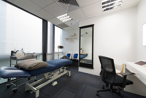 Interior of a chiropractic treatment room with chiropractic table, electrotherapy and ultrasound machine, with consulting table and bonds model.