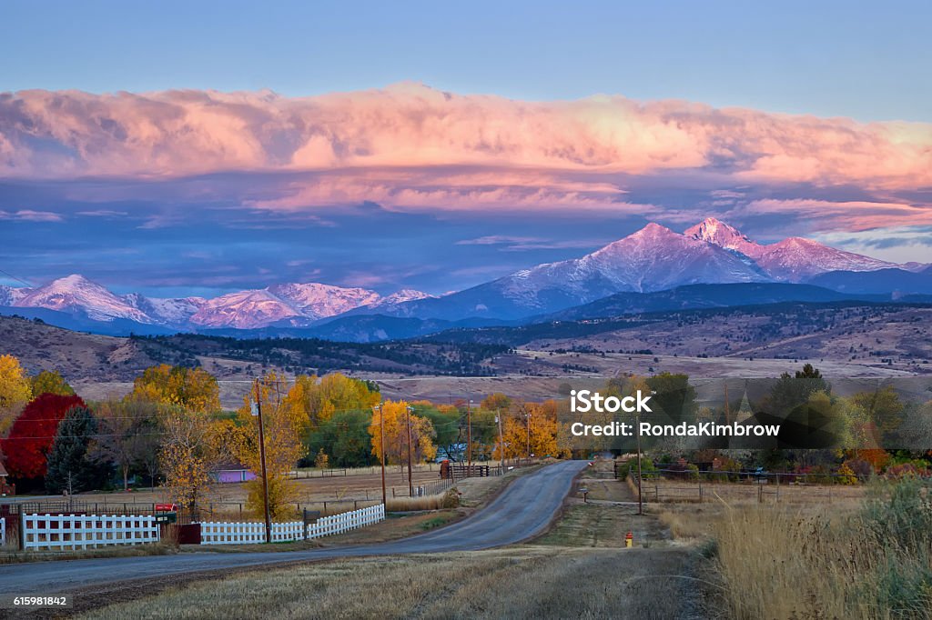 Long's Peak Sunrise on a Fall Morning Long's Peak lights up at sunrise as a rural country road leads into the fall trees Colorado Stock Photo