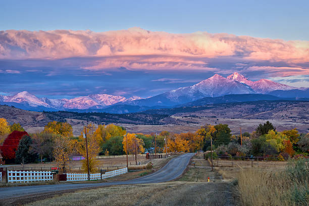 Long's Peak Sunrise on a Fall Morning Long's Peak lights up at sunrise as a rural country road leads into the fall trees front range mountain range stock pictures, royalty-free photos & images