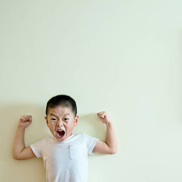 маленький мальчик, стоящий у стены, показывая свои мышцы - flexing muscles little boys human muscle strength стоковые фото и изображения