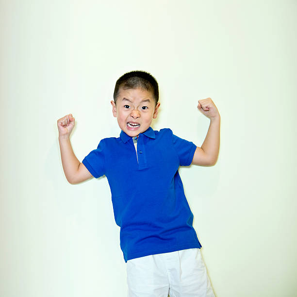 маленький мальчик, стоящий у стены, показывая свои мышцы - flexing muscles little boys human muscle strength стоковые фото и изображения