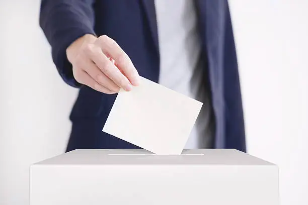 Man putting a ballot into a voting box.