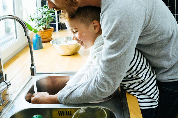 istock Father Washing Sons Hands In Kitchen Sink After Cooking Together 616012586