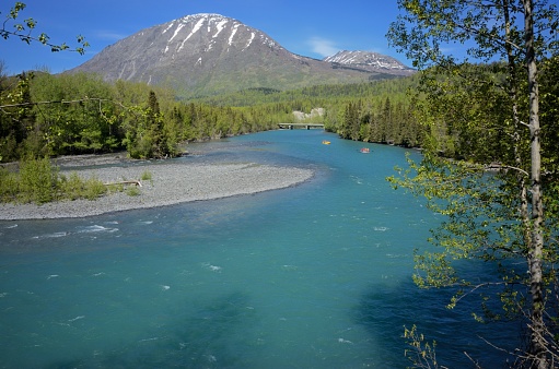 Looking up the Russian River in Alaska with snow covered mountain in background and unrecognizable rafters in tube rafts floating down the river.  Photograph taken in Alaska during the summer.
